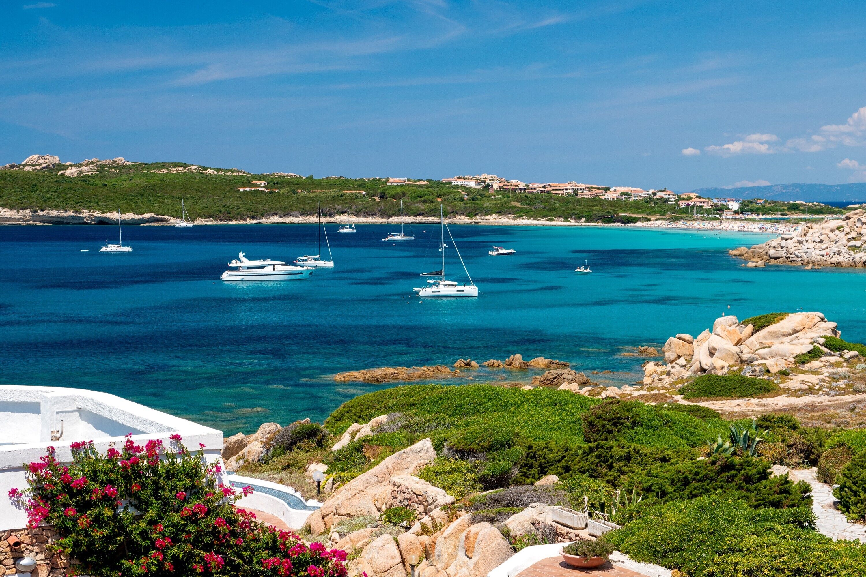 A coastal view with boats, rocky terrain, and greenery.