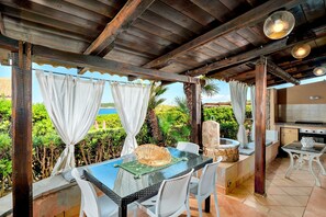 An outdoor dining area with a glass table, wicker chairs, and a view of the ocean. - Charming Villa with Sea View, Wi-Fi, Garden and Terrace (Santa Teresa Gallura)