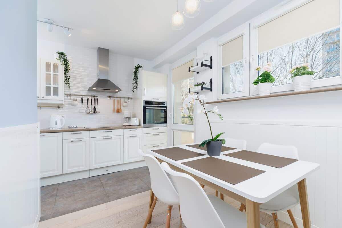 Una cocina moderna con armarios blancos, una mesa de comedor con sillas y una ventana con plantas en macetas.