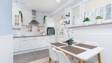 Een moderne keuken met witte kasten, een eettafel met stoelen en een raam met potplanten.