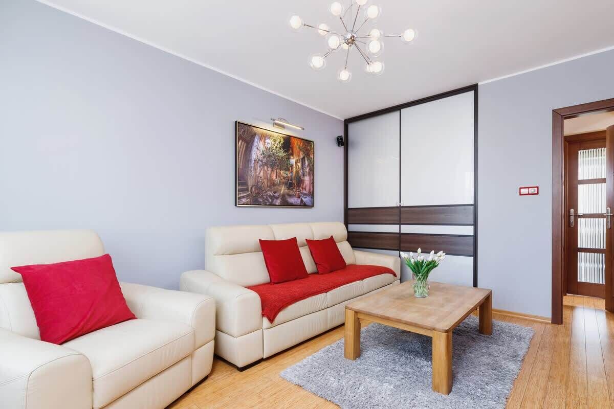 Ein modernes Wohnzimmer mit einem weißen Sofa, roten Kissen, einem Holztisch und einem Gemälde an der Wand.