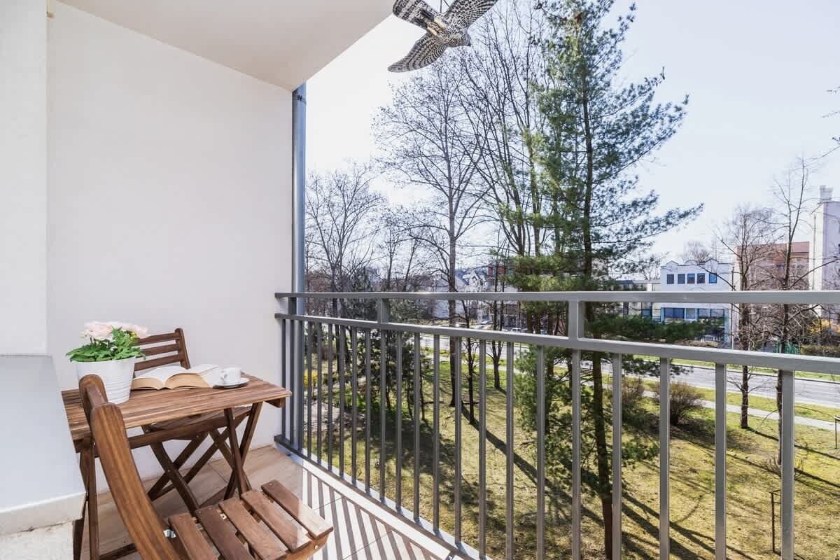 Ein Balkon mit Holztisch und -stühlen, einem Blumentopf und Blick auf Bäume und Gebäude.