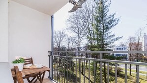 Parvekkeella on puinen pöytä ja tuolit, ruukkuistutettu kasvi sekä näkymä puihin ja rakennuksiin.