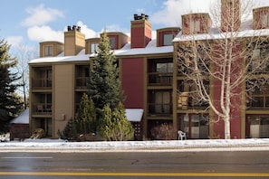 A multi-story building with a snow-covered roof, balconies, and a small tree in the foreground. - First Chair Snowcrest Base Camp | Walk to Lifts (Park City)