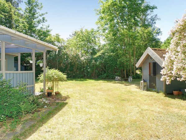 A rustic cabin with a covered porch and a small shed in a lush garden. - 5 Person Holiday Home in Eskebjerg (Eskebjerg)