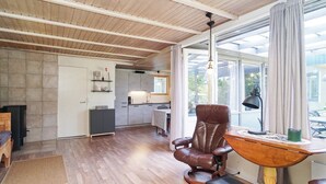 Um quarto espaçoso com piso de madeira, uma mesa de jantar com cadeiras, lareira e uma grande janela com cortinas.