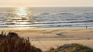 Una spiaggia con una persona che va in bicicletta, le onde e il sole che tramonta sull'oceano.