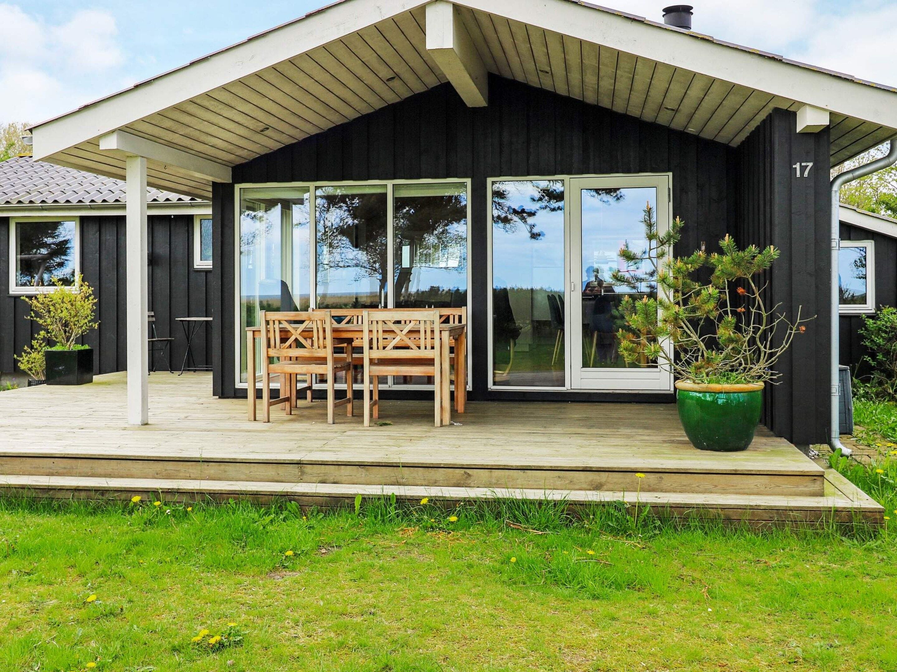 A modern house with a covered porch, a dining table with chairs, and a large green potted plant.