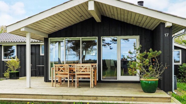 A modern house with a covered porch, large sliding glass doors, and a wooden table and chairs. - Cozy Holiday Home in Hadsund near Sea (Hadsund)