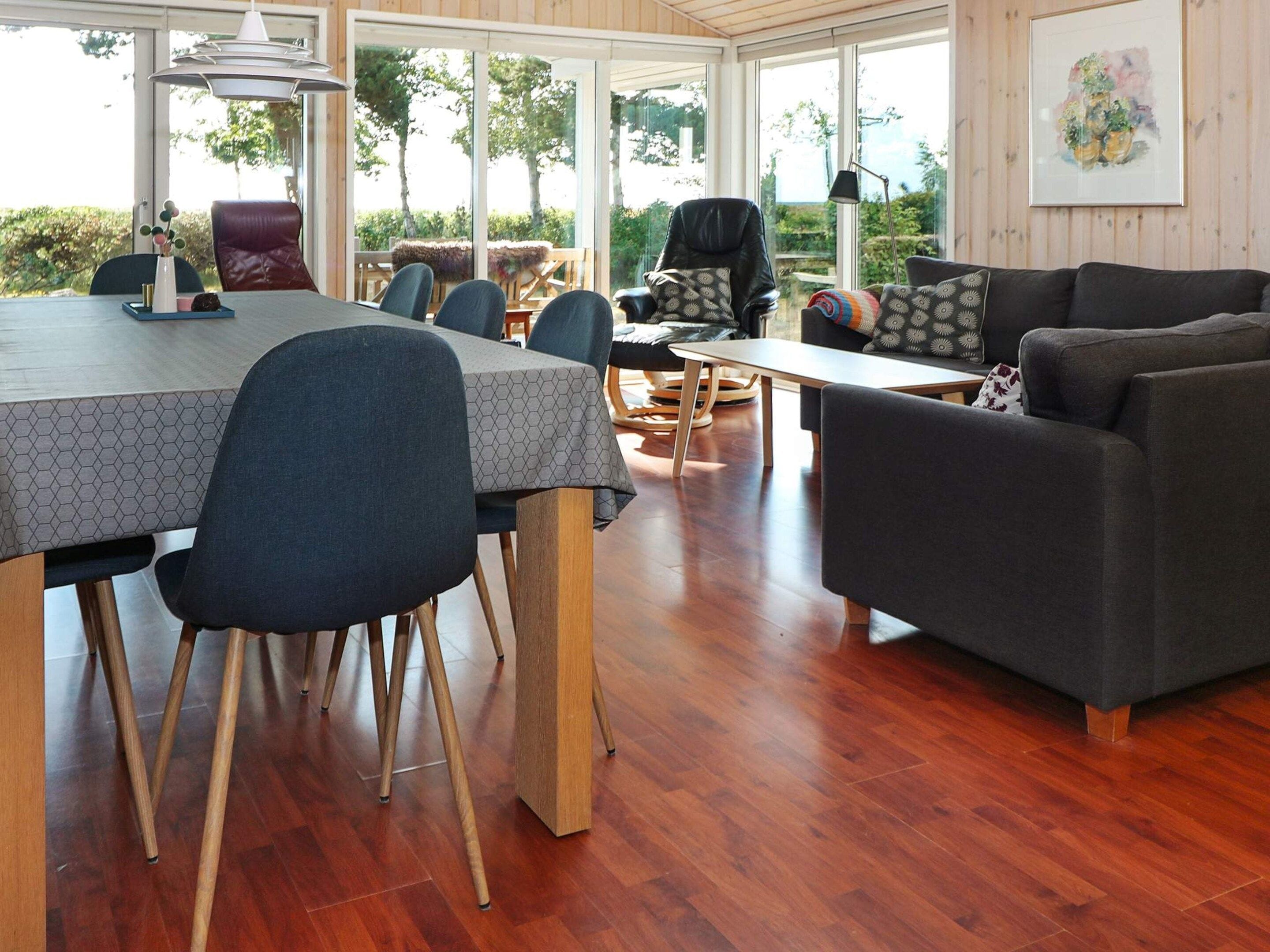 A spacious room with a dining table, chairs, a sofa, and a large window offering a view of greenery.