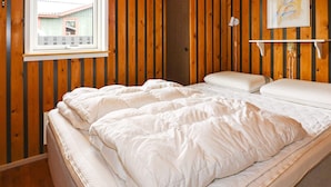 A bedroom with a wooden paneled wall, a window, a bed with white bedding, and a white shelf with a painting. - Cozy Holiday Home in Hadsund near Sea (Hadsund)