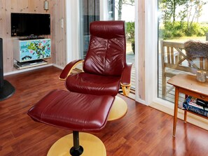 Un fauteuil inclinable en cuir rouge avec un repose-pieds, un téléviseur posé sur un meuble en bois et une bibliothèque remplie de livres.