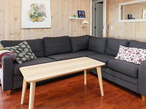A modern living room with a grey sectional sofa, a wooden coffee table, and a framed floral painting on the wall. - Cozy Holiday Home in Hadsund near Sea (Hadsund)