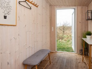 A wooden room with a bench, a door leading outside, and a small table with a plant.