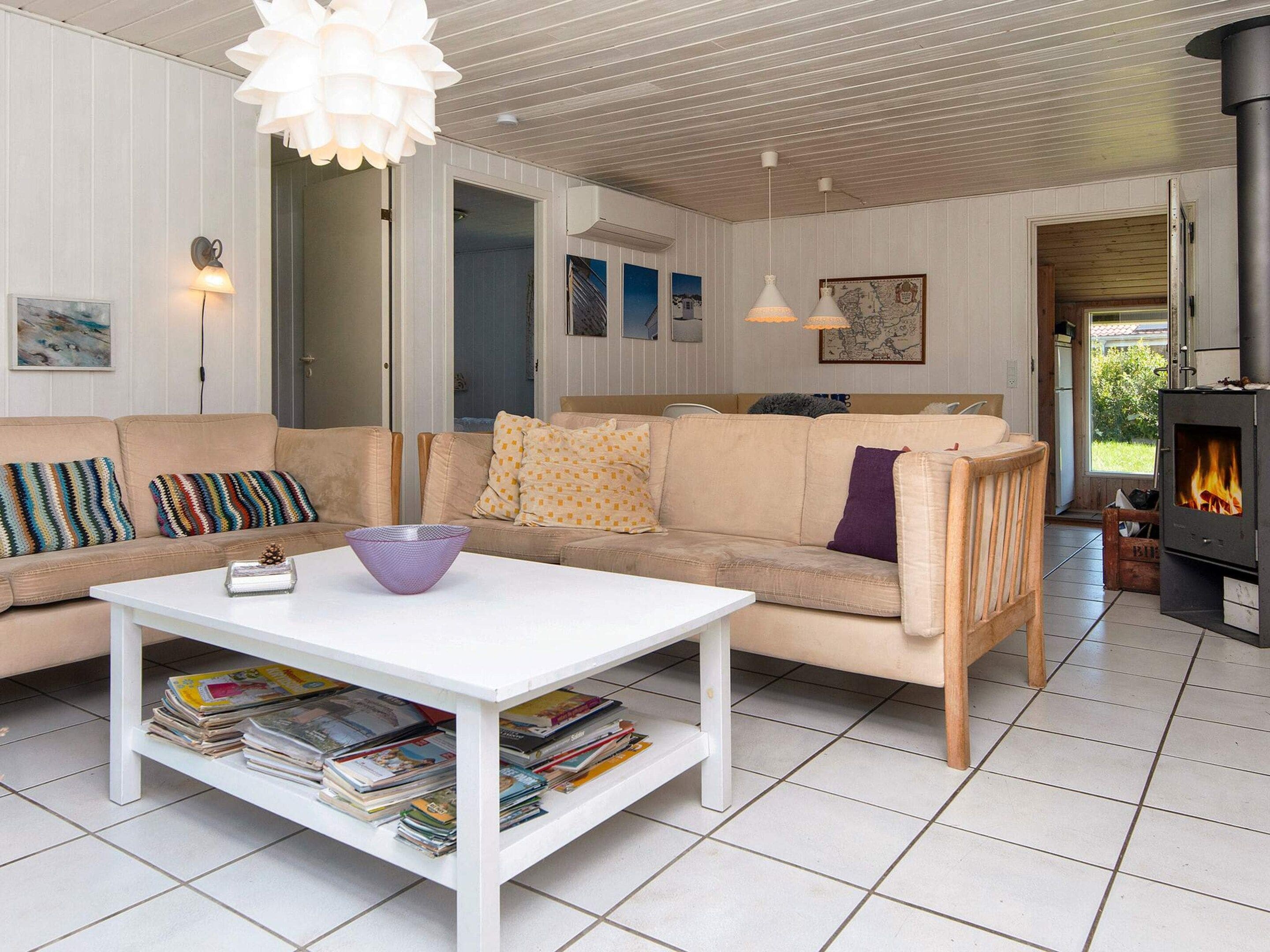 A cozy living room with a sofa, a white coffee table with magazines, a fireplace, and a view of the outdoors.