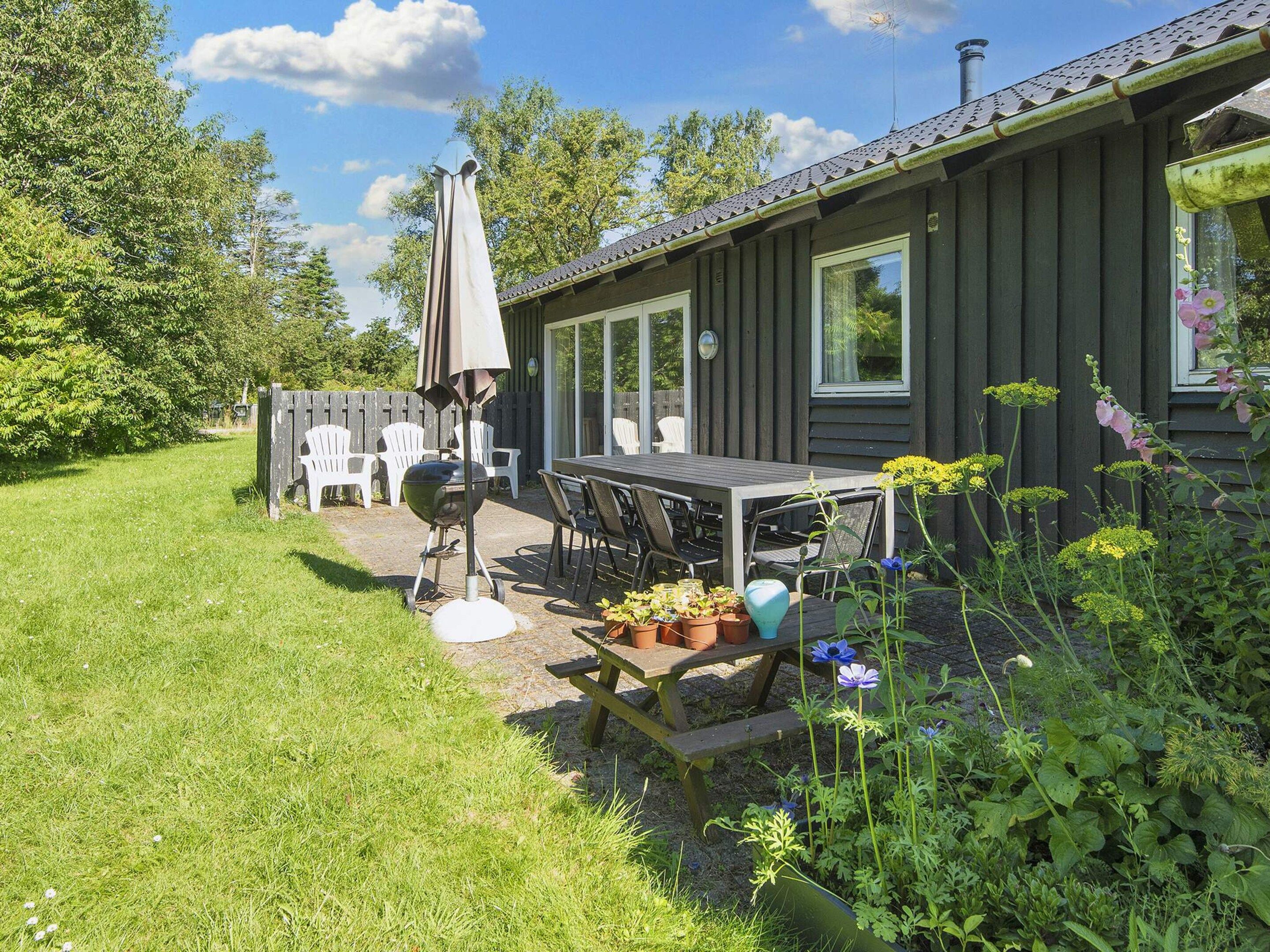 Una casa de madera con un patio, mobiliario exterior y una parrilla.