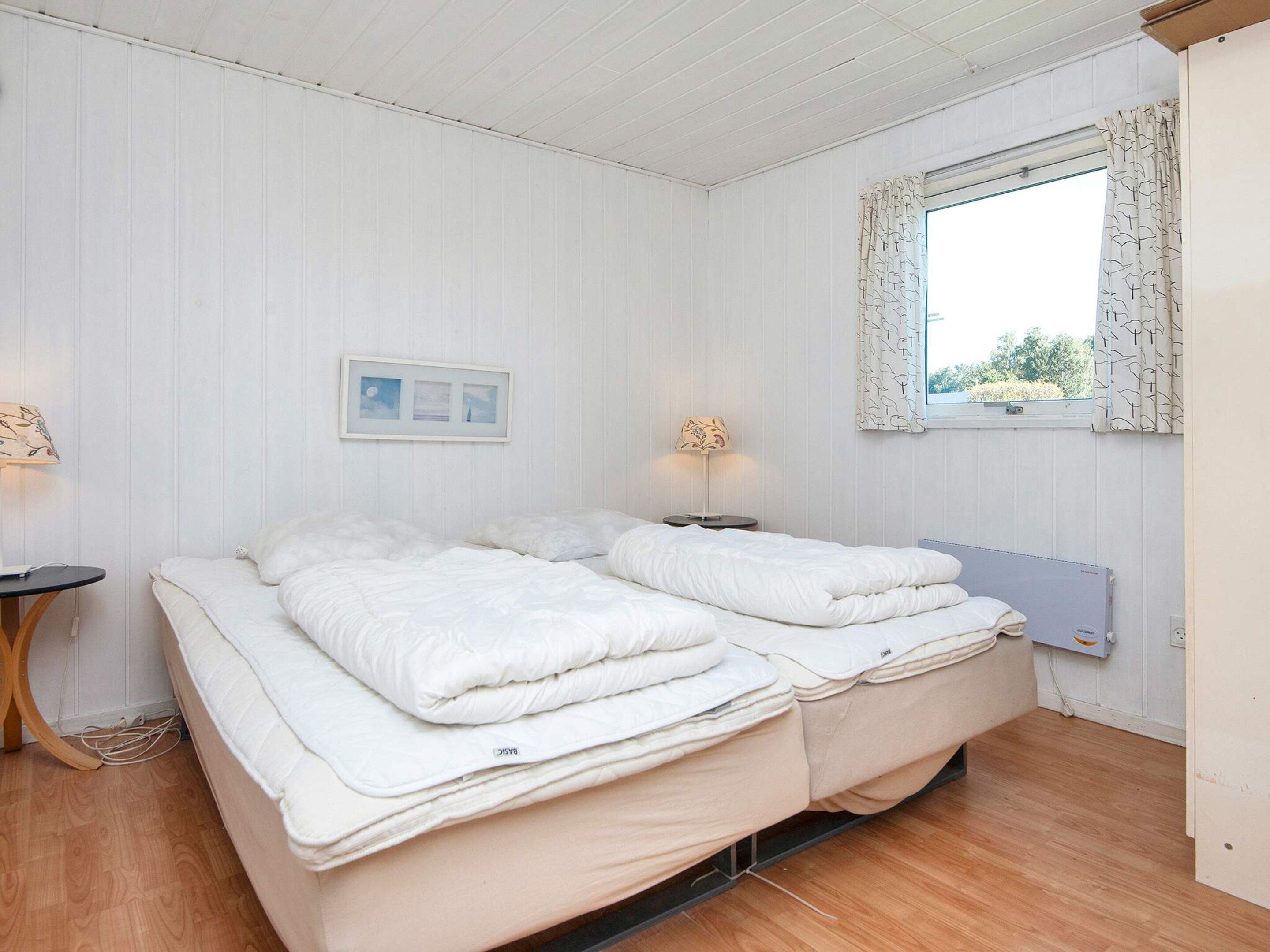 A double bed with a headboard, a bedside table, a lamp, and a window with curtains.