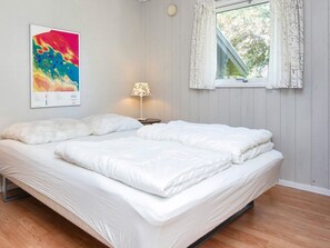 A neatly made bed with white bedding, a lamp on a bedside table, and a colorful abstract painting on the wall.