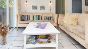A cozy living room with a white coffee table, two sofas with colorful cushions, and a bookshelf filled with magazines.