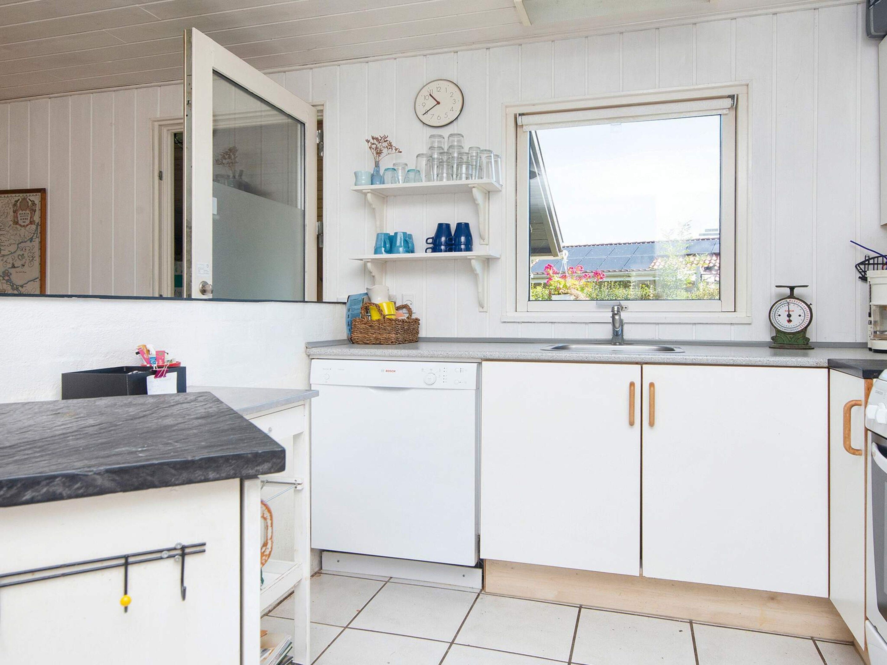 Una cocina con armarios blancos, un lavavajillas Bosch, una ventana con vistas y un reloj en la pared.