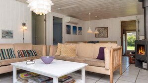 A cozy living room with a beige sofa, a white coffee table with magazines, a fireplace, and a view of the outdoors.