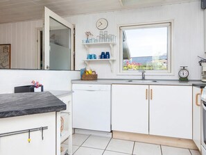 A kitchen with white cabinets, a Bosch dishwasher, a window with a view, and a clock on the wall.