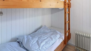 Un lit superposé avec une structure en bois et une échelle, des murs blancs et un radiateur.