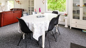 Un coin repas avec une table ronde, des chaises noires et une nappe blanche. On aperçoit, à l’arrière-plan, un canapé rouge et un meuble avec des portes en verre.