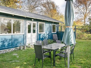 A blue house with a patio area featuring a table and chairs, a covered umbrella, and a small garden.