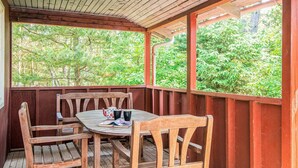 Eine Holzdar Terrasse mit Tisch und Stühlen, umgeben von einem Geländer, mit Blick auf eine üppige grüne Landschaft.