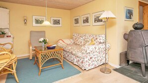 A cozy living room with a floral sofa, a wicker table with a vase, and a grey armchair. - 7 Person Holiday Home in Jerup (Strandby)