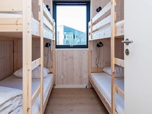 Une chambre avec un lit superposé, une fenêtre, des murs en bois et une porte.