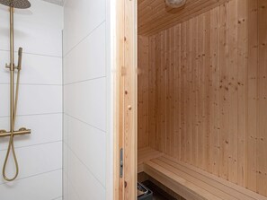 A wooden sauna with a bench and a shower area with a gold showerhead and hose. - 5 Star Holiday Home in Glesborg (Glesborg)