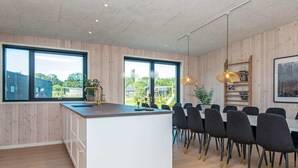 Een moderne keuken met een centraal eiland, een eetgedeelte met stoelen en grote ramen.