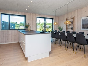 Une cuisine moderne dotée d’un îlot central, de grandes fenêtres et d’un coin repas avec des chaises.