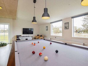 A pool table with balls, a television, and chairs in a room with windows. - 5 Star Holiday Home in Oster Assels (Øster Assels)