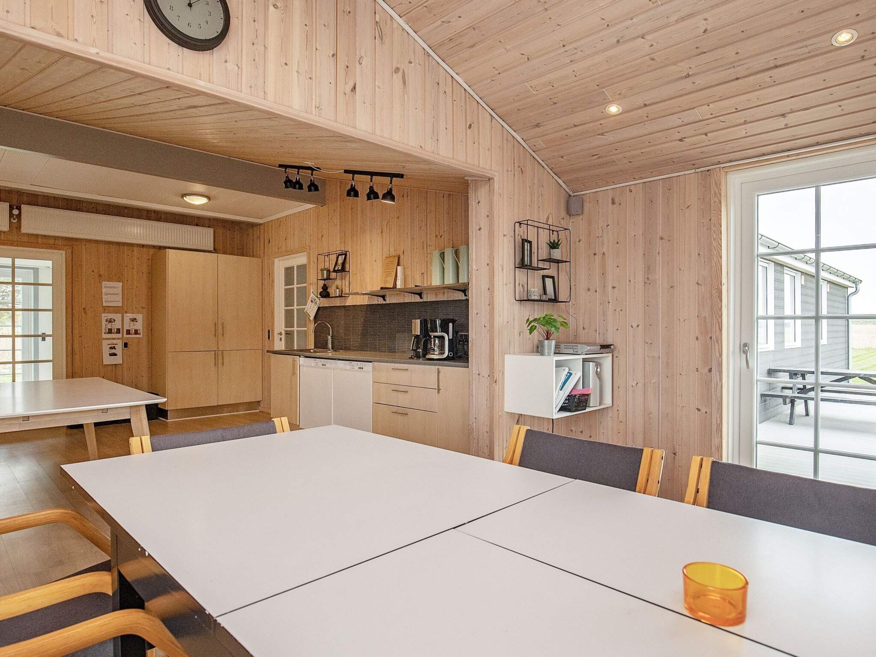 A modern kitchen with wooden paneling, a dining area with a large table, and a view through a glass door.