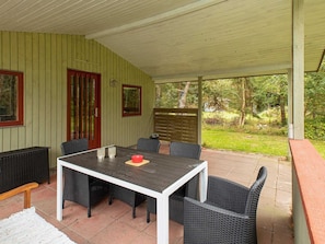 A covered patio with a table and chairs, a red door, and a view of the garden.