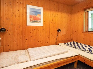 A wooden cabin room with a single bed, a framed picture on the wall, and a window.