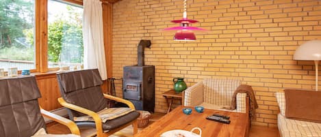 A cozy room with a brick wall, a wooden ceiling, a table with chairs, a sofa, and a fireplace.