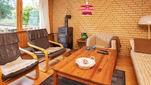 Um quarto acolhedor com parede de tijolos, teto de madeira, lareira, uma mesa com uma cesta e duas cadeiras.