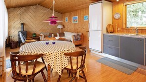 Interior acolhedor de uma cabana, com mesa de jantar, cadeiras, sofá, área de cozinha e lareira.