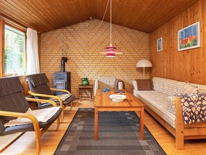 A cozy living room with a brick wall, wooden ceiling, a sofa, two armchairs, a coffee table, and a fireplace.