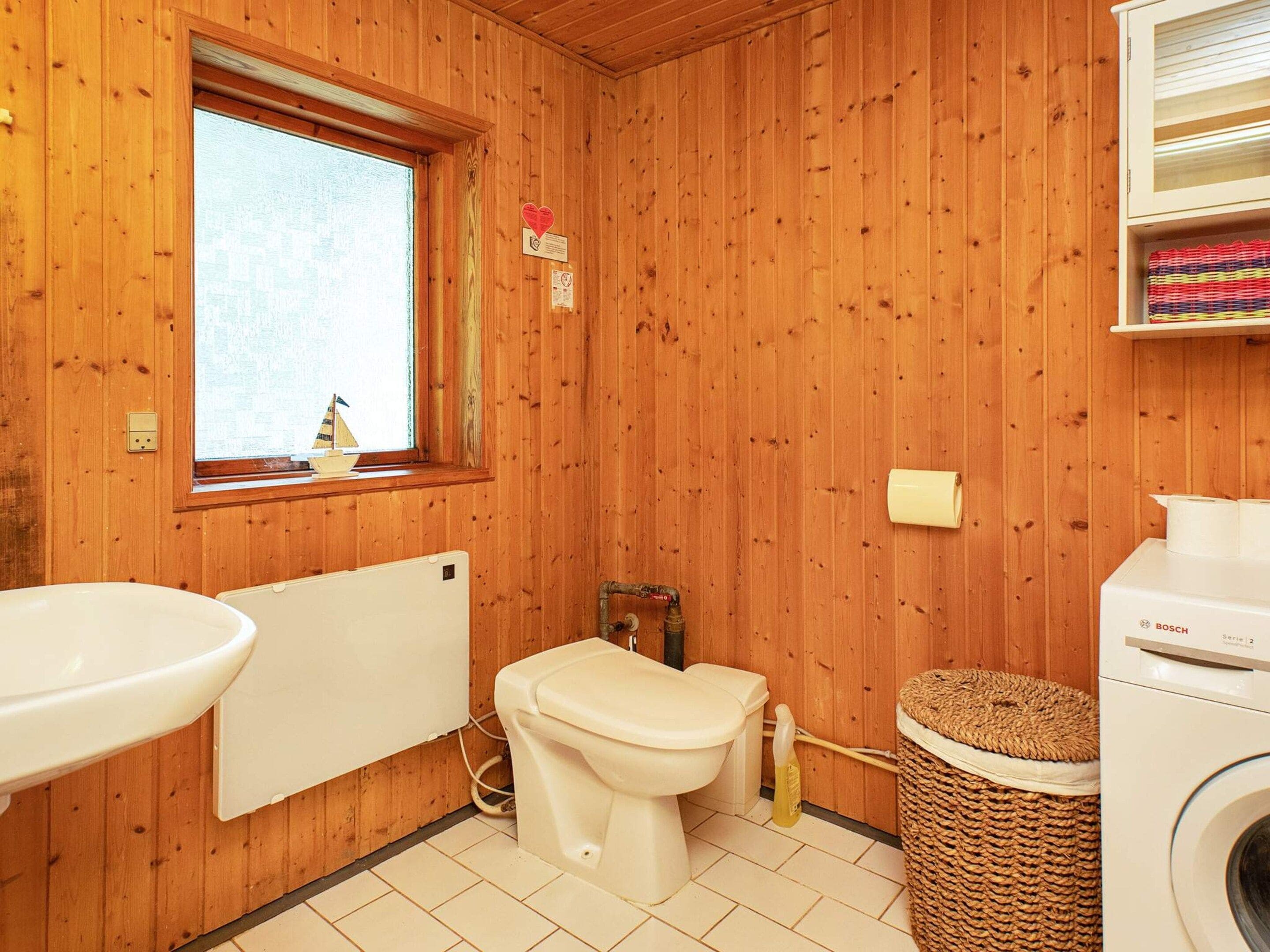 A wooden-paneled bathroom with a toilet, sink, and a washing machine.