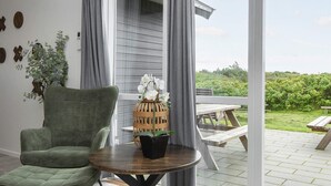 A room with a green armchair, a round table with a potted plant, and a view of a patio with a wooden table and benches. - 4 Star Holiday Home in Harboore (Harboore)