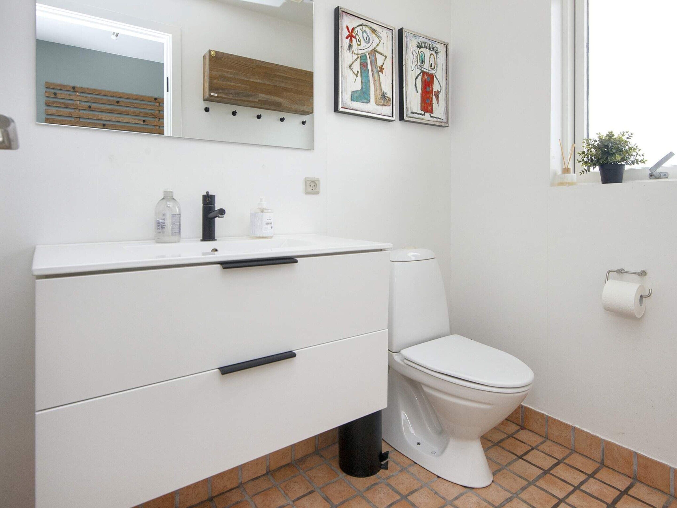 A bathroom with a white sink, a mirror, a toilet, and two children's drawings on the wall.