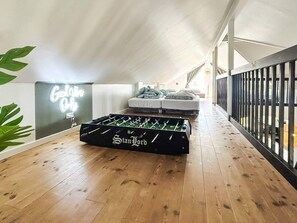 Et hyggeligt loftværelse med et bordtennisbord, en seng med puder og en neonlysende vægdekoration.