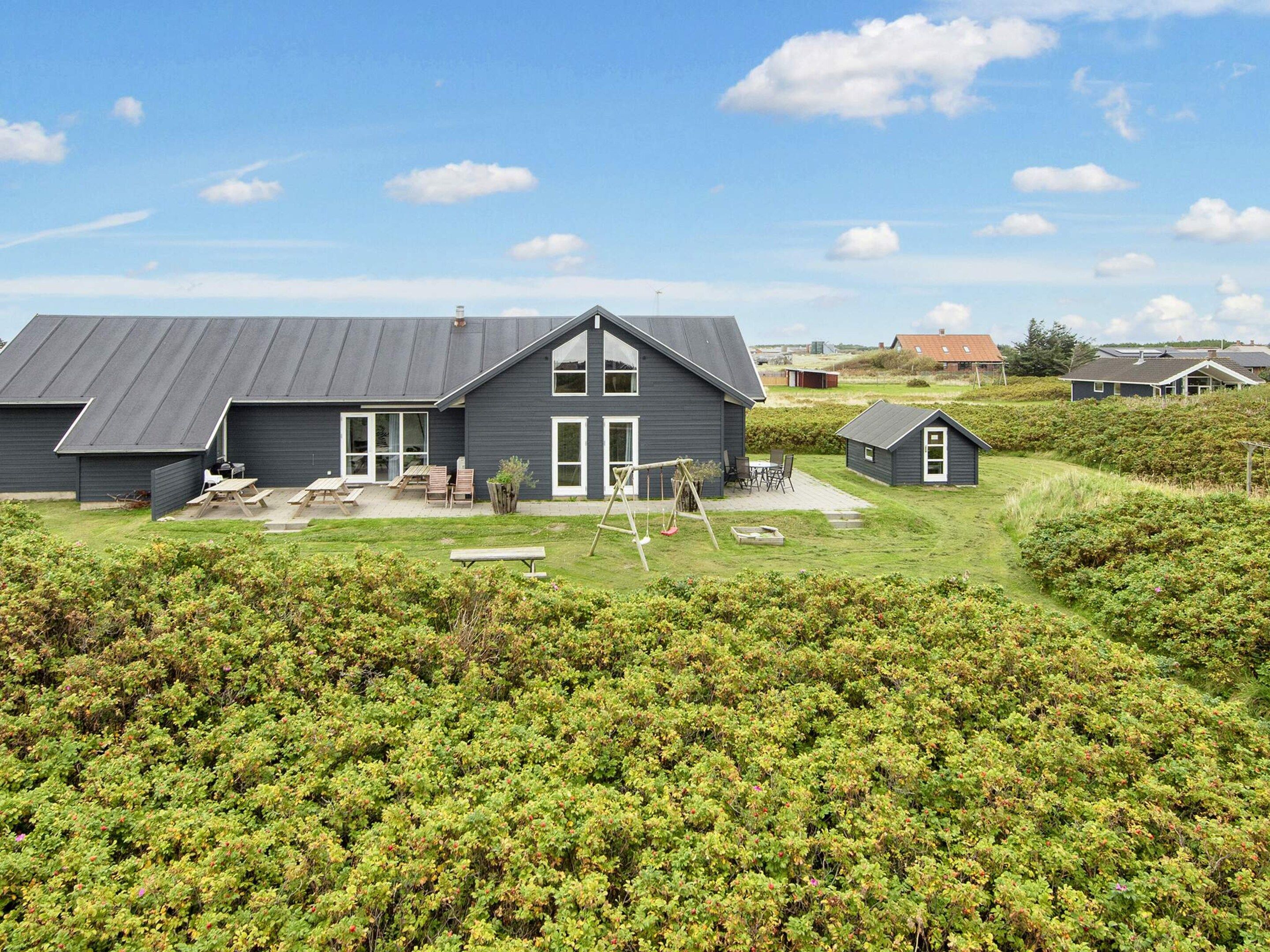 Une maison à deux étages avec un grand jardin devant, une balançoire et un petit abri de jardin.