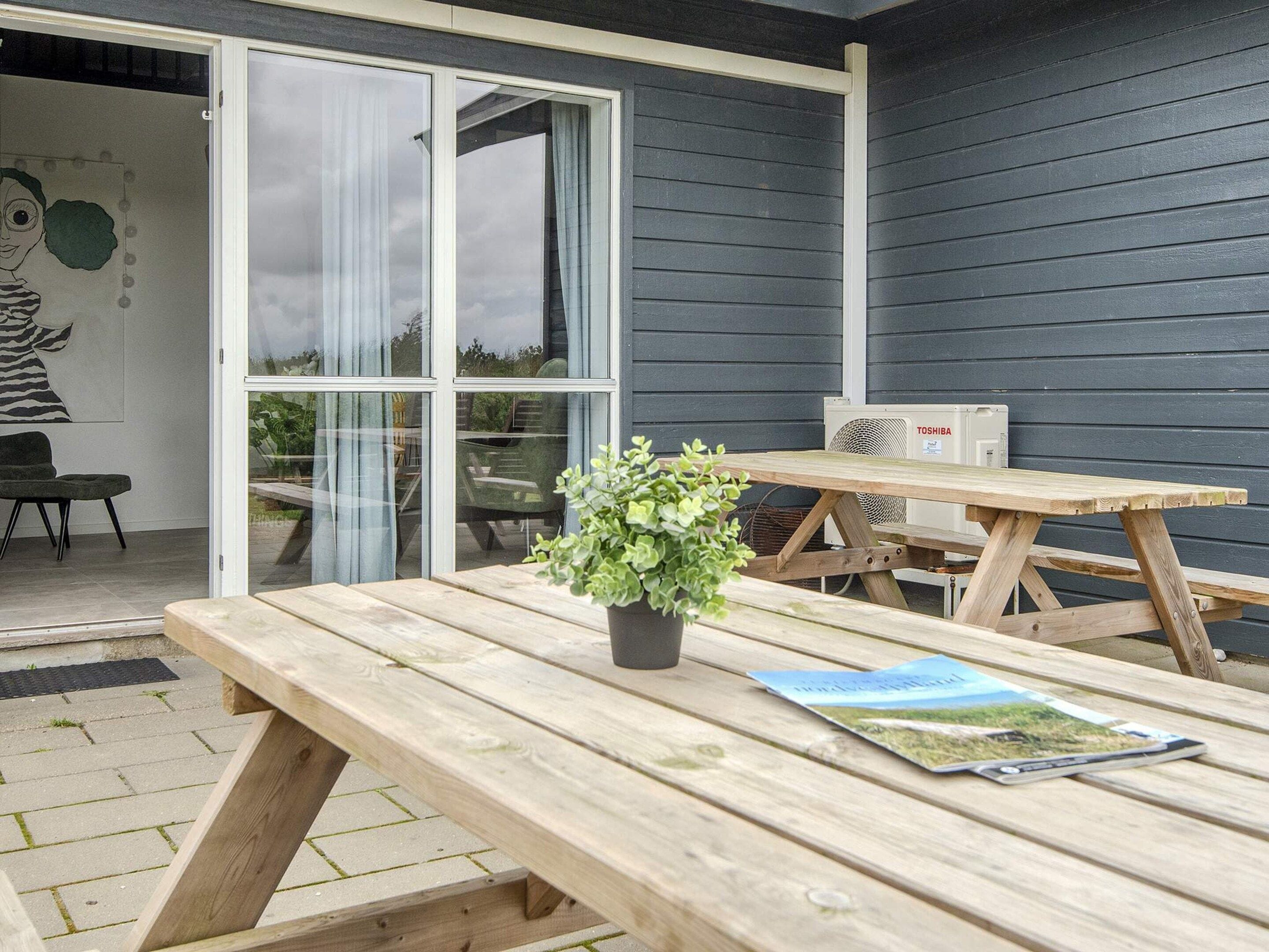 Un patio al aire libre con una mesa de madera, una planta en maceta y un aire acondicionado Toshiba contra una pared oscura.