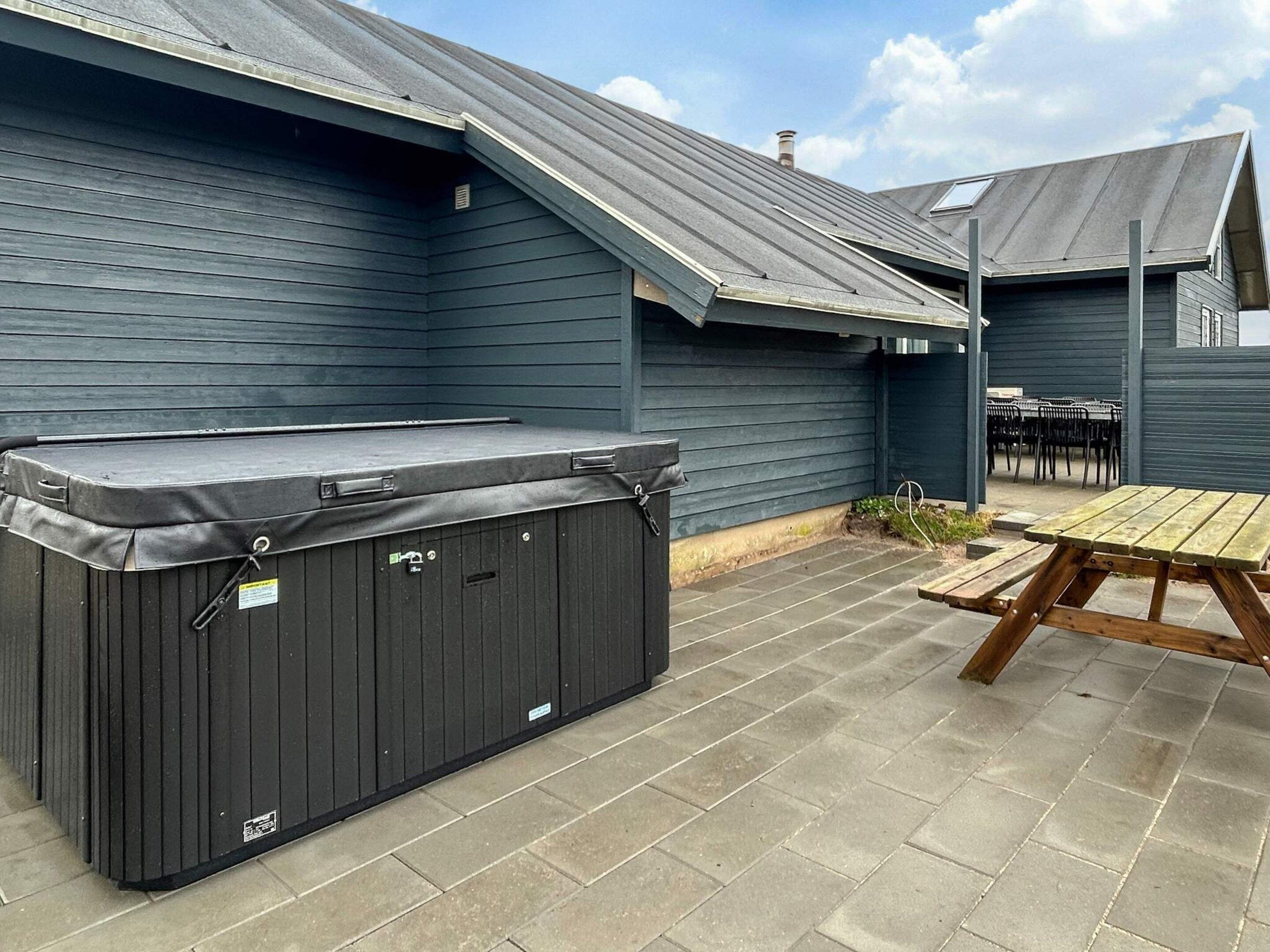 A covered outdoor area with a hot tub, picnic table, and chairs.